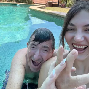 A participant and support worker laughing together in a swimming pool