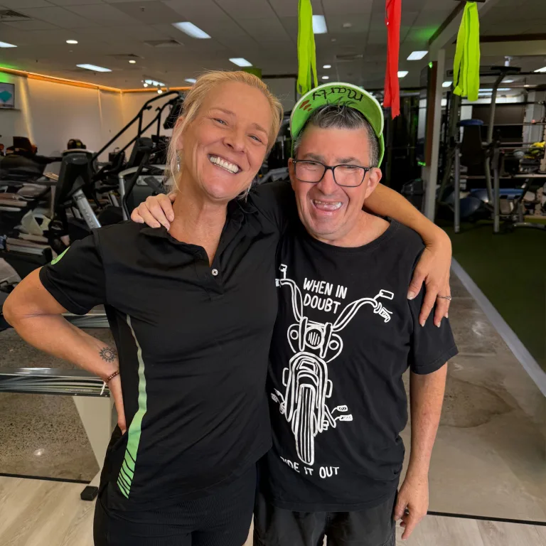 A participant and support worker smiling together at the gym