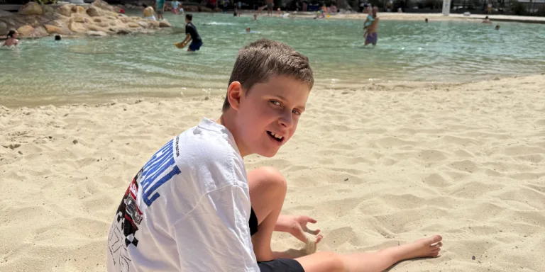 A boy sitting on the sand at a lagoon beach